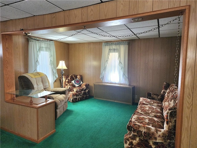 sitting room with a paneled ceiling, wooden walls, radiator, and carpet