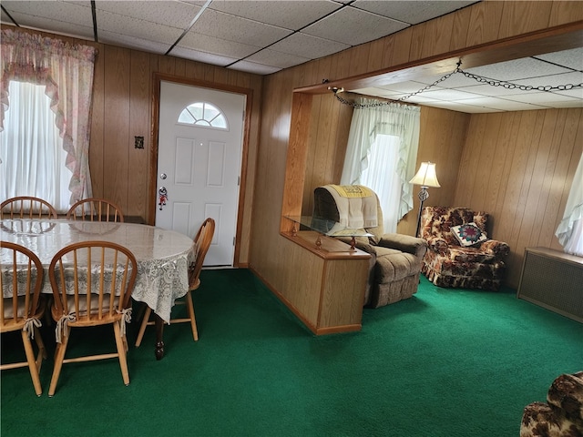 carpeted dining room featuring radiator, wood walls, and a drop ceiling