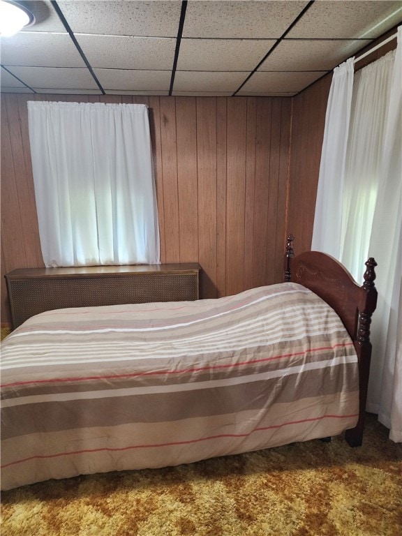 bedroom with wood walls, a paneled ceiling, and carpet