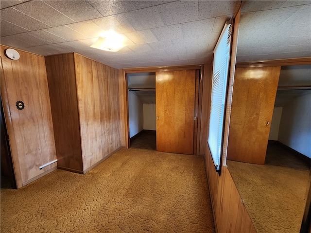 unfurnished bedroom featuring a closet, wood walls, and carpet floors