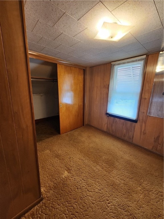 unfurnished bedroom featuring wooden walls, carpet floors, and a closet