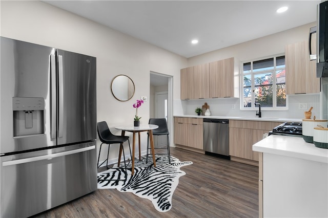 kitchen with appliances with stainless steel finishes, light brown cabinetry, dark wood-type flooring, and sink