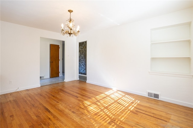 empty room featuring a notable chandelier, hardwood / wood-style floors, and built in features