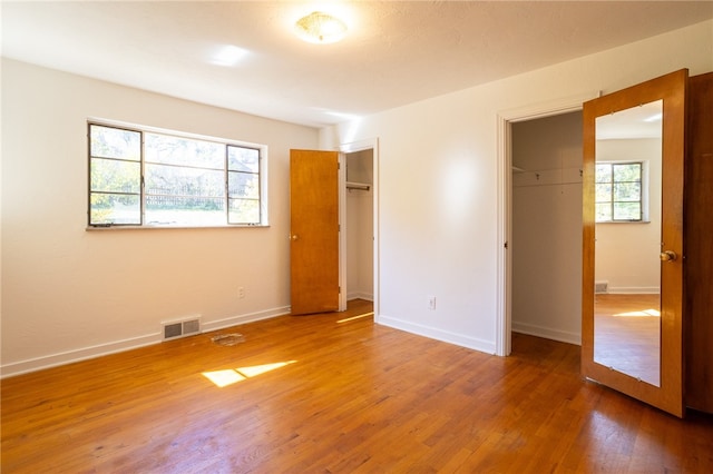 unfurnished bedroom featuring multiple windows, hardwood / wood-style floors, and a closet