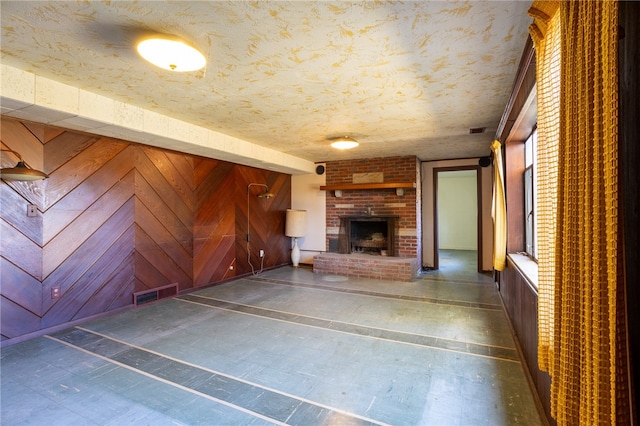 unfurnished living room featuring a textured ceiling, wooden walls, and a brick fireplace