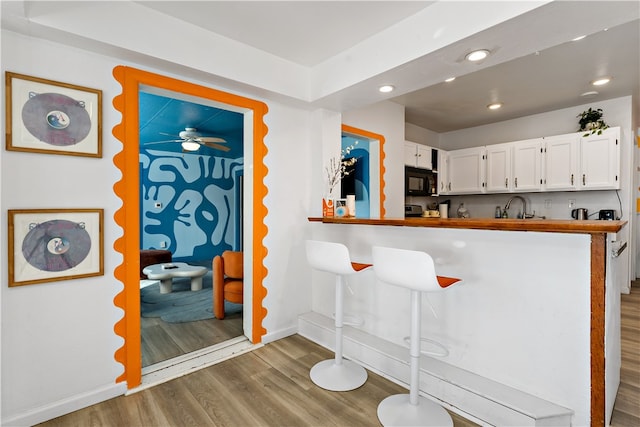 kitchen with kitchen peninsula, hardwood / wood-style floors, white cabinets, ceiling fan, and sink