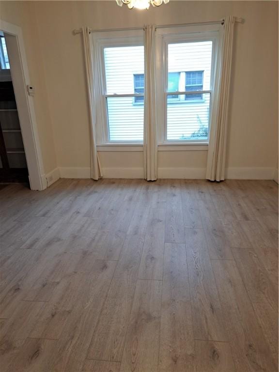 spare room featuring light wood-type flooring and a chandelier