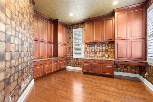 unfurnished office featuring built in desk, a textured ceiling, and hardwood / wood-style floors