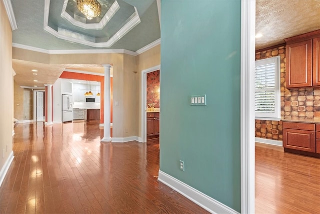 corridor with ornate columns, crown molding, wood-type flooring, and a raised ceiling