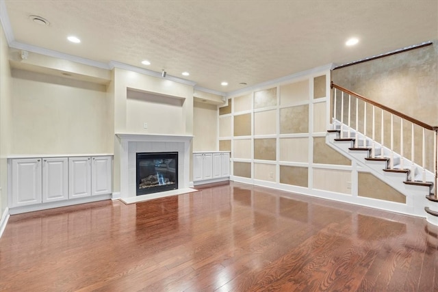 unfurnished living room with a textured ceiling, crown molding, wood-type flooring, and a tile fireplace