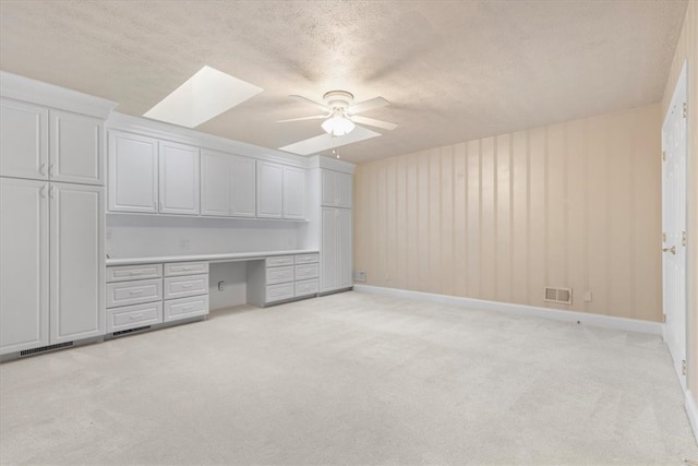 unfurnished office featuring light carpet, built in desk, ceiling fan, a textured ceiling, and a skylight