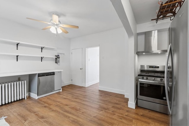 kitchen with radiator, wall chimney exhaust hood, appliances with stainless steel finishes, and light wood-type flooring