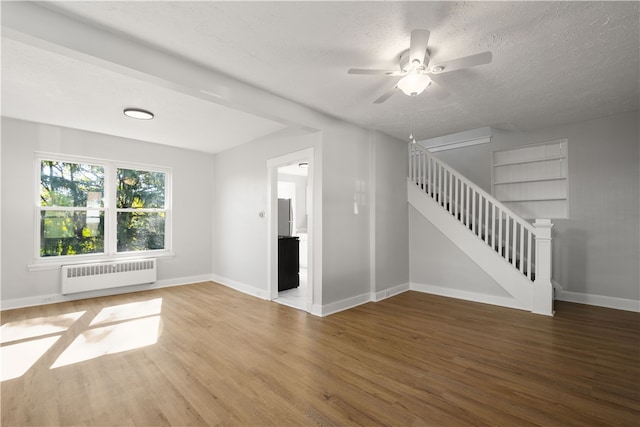 unfurnished living room featuring a textured ceiling, wood-type flooring, radiator, and ceiling fan