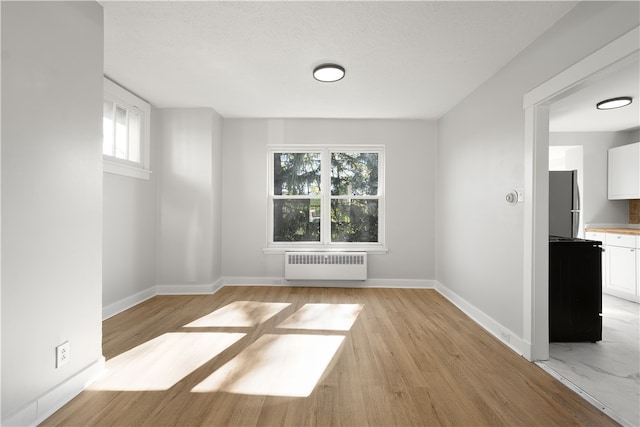 unfurnished room featuring light hardwood / wood-style flooring, a textured ceiling, and radiator