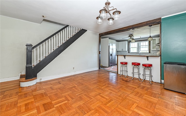 unfurnished living room with light parquet floors, ceiling fan with notable chandelier, and wet bar