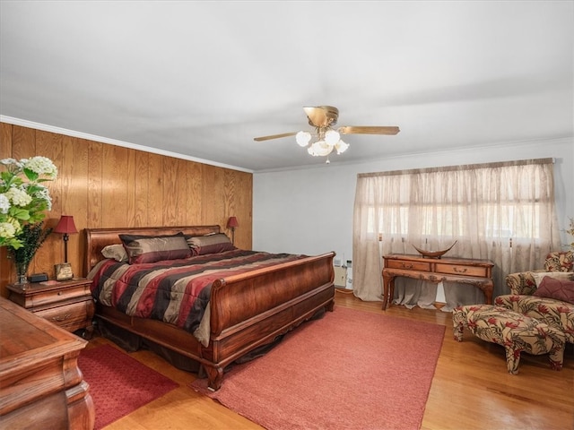 bedroom featuring wood walls, crown molding, light hardwood / wood-style floors, and ceiling fan