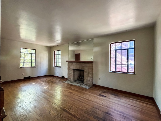 unfurnished living room featuring hardwood / wood-style flooring and a stone fireplace