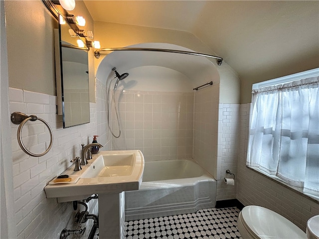 bathroom featuring toilet, lofted ceiling, tiled shower / bath combo, and tile walls