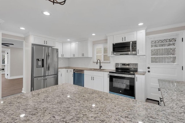 kitchen with light stone counters, stainless steel appliances, crown molding, and white cabinetry