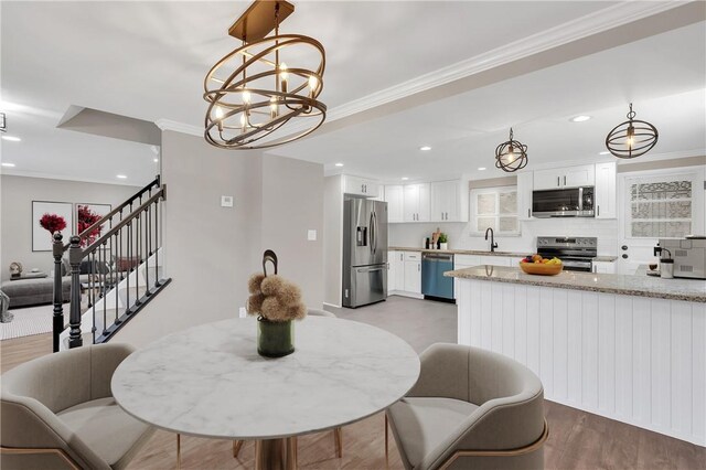 dining room with sink, a notable chandelier, crown molding, and light wood-type flooring