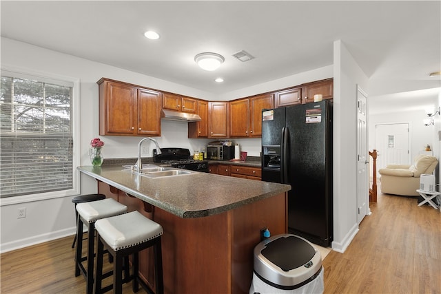 kitchen featuring black appliances, sink, light hardwood / wood-style flooring, a kitchen bar, and kitchen peninsula