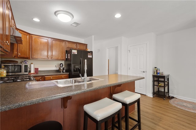 kitchen featuring a kitchen breakfast bar, light hardwood / wood-style flooring, appliances with stainless steel finishes, kitchen peninsula, and extractor fan