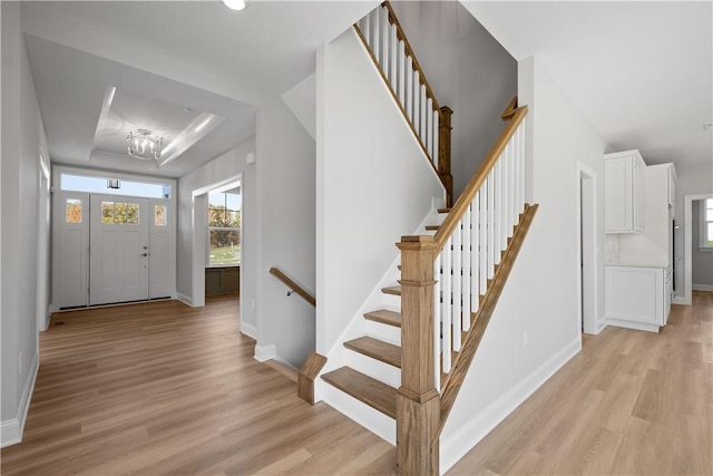 foyer with an inviting chandelier, light hardwood / wood-style flooring, and a tray ceiling