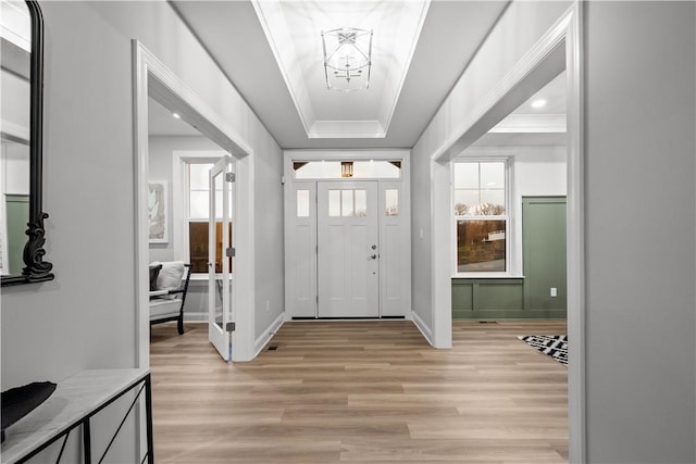 entryway with an inviting chandelier, light wood-type flooring, and a tray ceiling