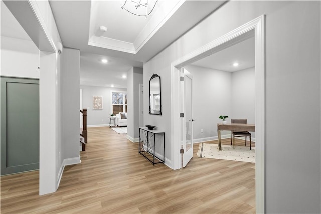 hallway with a tray ceiling and light hardwood / wood-style flooring