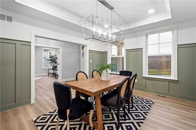 dining space with a chandelier, light wood-type flooring, a raised ceiling, and ornamental molding