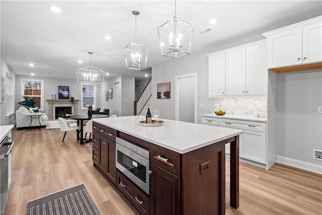 kitchen with tasteful backsplash, dark brown cabinetry, stainless steel appliances, decorative light fixtures, and white cabinetry