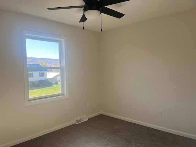 empty room featuring a wealth of natural light, dark carpet, and ceiling fan