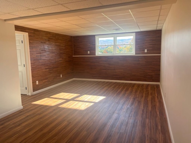 empty room featuring wood walls, dark hardwood / wood-style flooring, and a drop ceiling