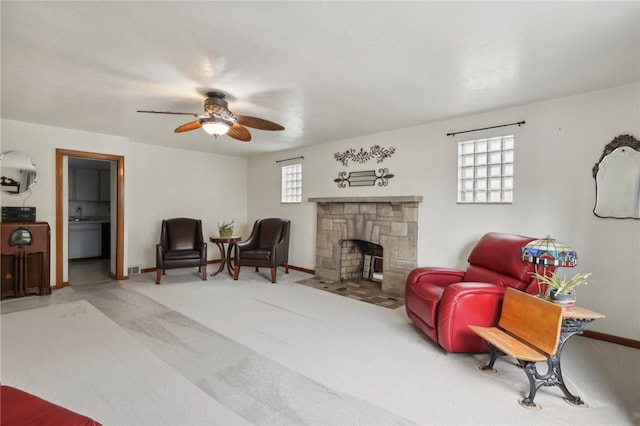 sitting room with ceiling fan, a healthy amount of sunlight, carpet, and a stone fireplace