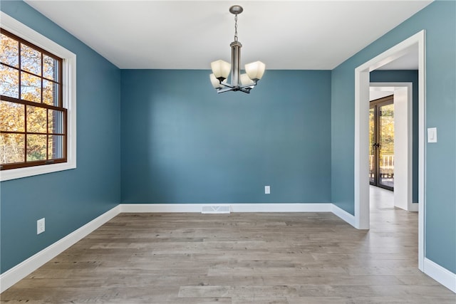 spare room with a wealth of natural light, a chandelier, and light hardwood / wood-style flooring