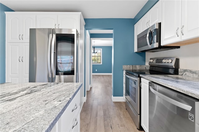 kitchen with light stone countertops, white cabinetry, light hardwood / wood-style flooring, and stainless steel appliances