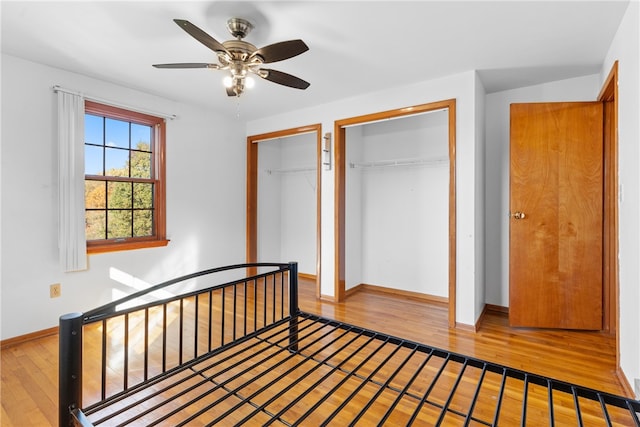 unfurnished bedroom with ceiling fan, hardwood / wood-style flooring, and two closets