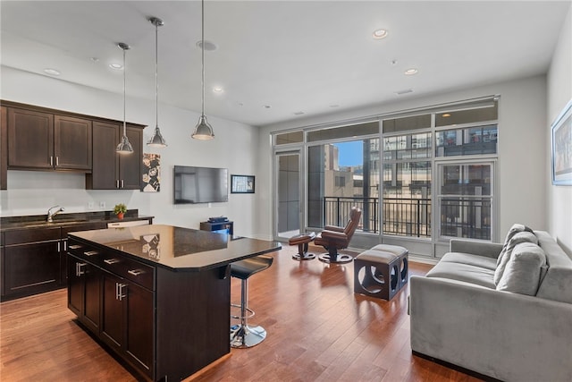 kitchen with a kitchen bar, a kitchen island, hanging light fixtures, dark brown cabinetry, and dark hardwood / wood-style floors