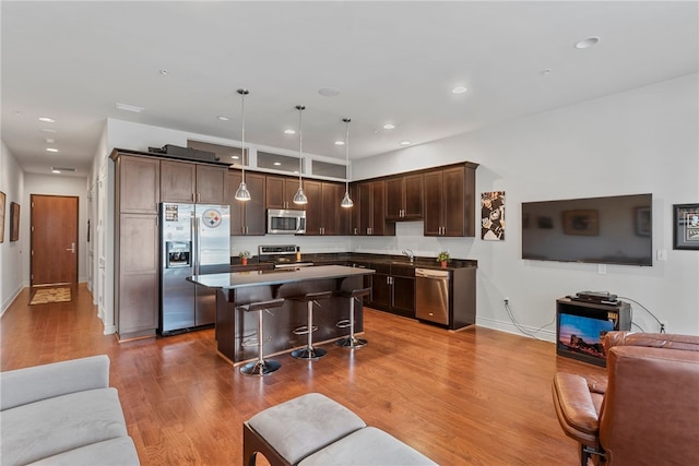 kitchen featuring appliances with stainless steel finishes, a kitchen bar, a kitchen island, hardwood / wood-style floors, and pendant lighting