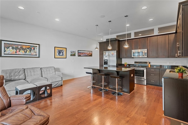 kitchen featuring a kitchen island, a kitchen breakfast bar, stainless steel appliances, pendant lighting, and light wood-type flooring