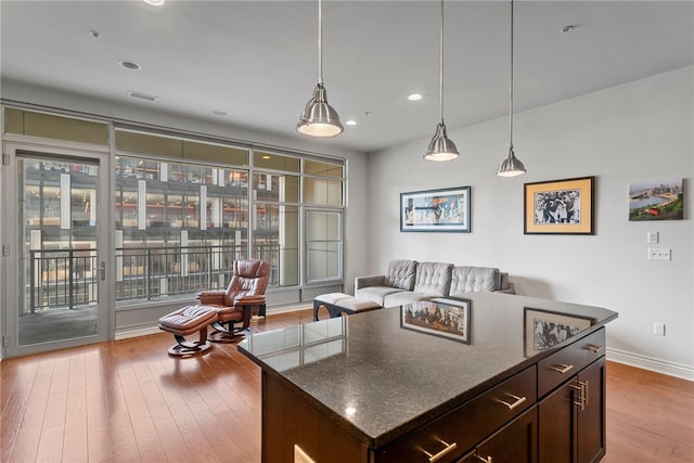 kitchen featuring a kitchen island, dark brown cabinets, light wood-type flooring, and dark stone countertops