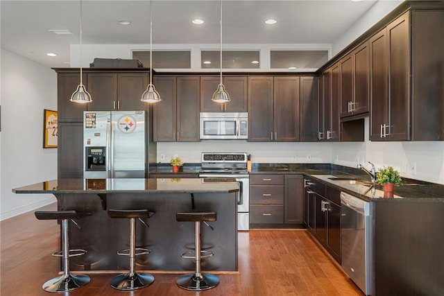 kitchen with a kitchen island, hanging light fixtures, light hardwood / wood-style floors, stainless steel appliances, and dark stone countertops