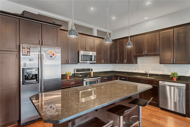 kitchen featuring a kitchen breakfast bar, hanging light fixtures, light hardwood / wood-style floors, stainless steel appliances, and dark stone countertops