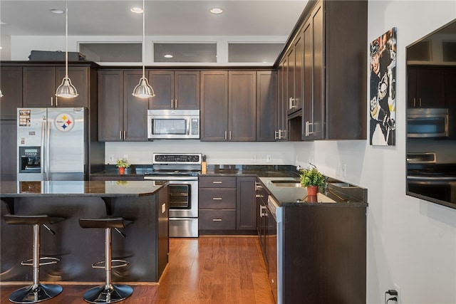 kitchen featuring appliances with stainless steel finishes, a kitchen island, dark hardwood / wood-style flooring, pendant lighting, and dark stone countertops