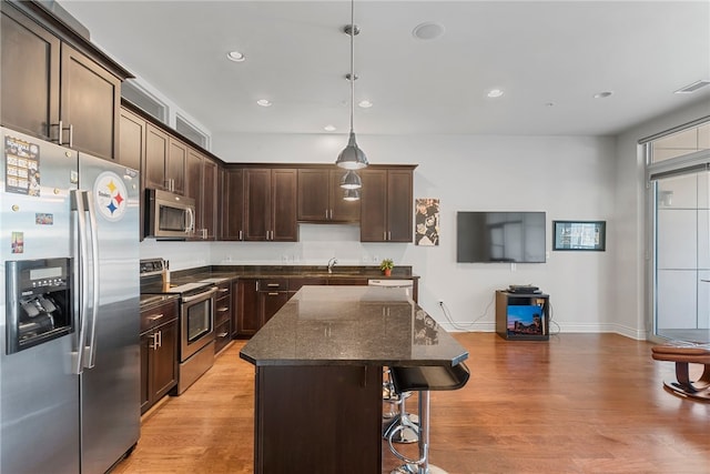 kitchen featuring dark stone counters, light hardwood / wood-style flooring, stainless steel appliances, decorative light fixtures, and a center island