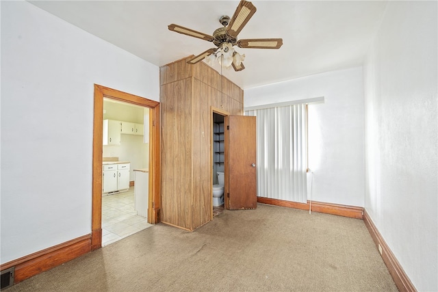 unfurnished bedroom featuring wood walls, ceiling fan, ensuite bathroom, and light colored carpet