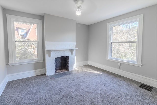 unfurnished living room with a wealth of natural light, a fireplace, carpet flooring, and ceiling fan