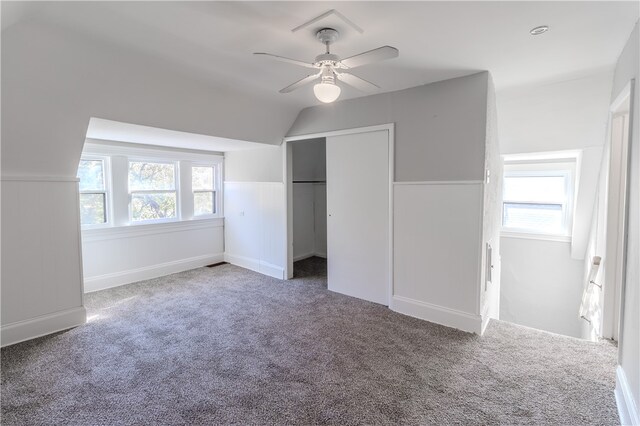 unfurnished bedroom featuring ceiling fan, lofted ceiling, multiple windows, and dark colored carpet