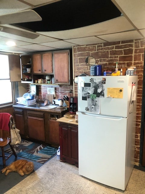 kitchen with a drop ceiling, white fridge, sink, and brick wall