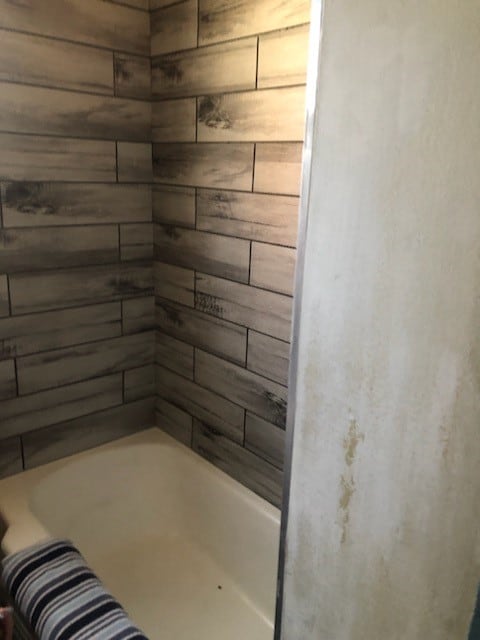 bathroom with a tub to relax in and wood walls